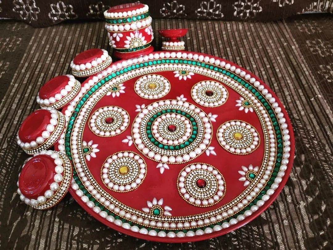 Red pooja thali decorated with white pearl mandalas, turquoise stones and floral patterns