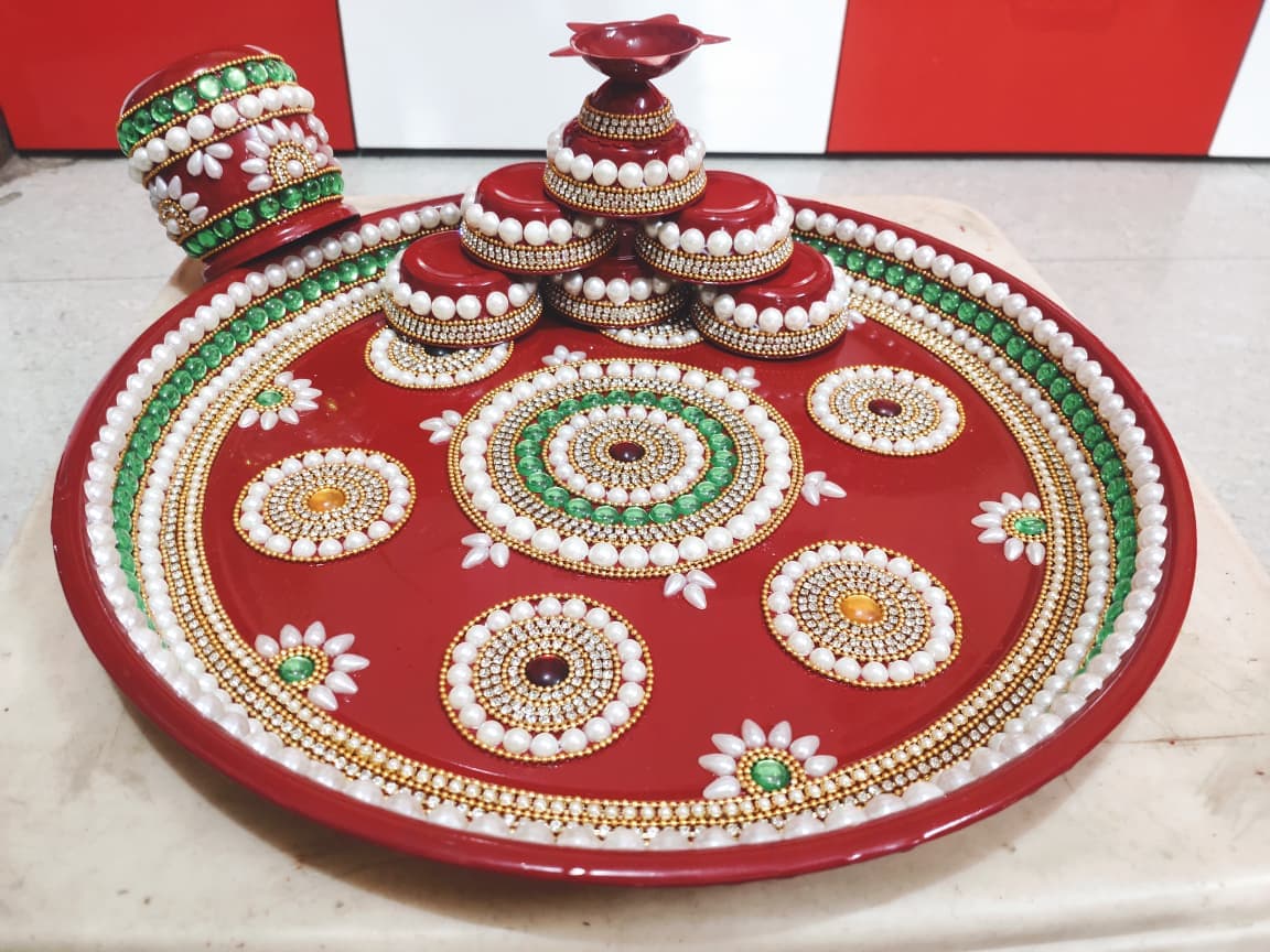 Red pooja thali with circular pearl patterns, emerald accents, kumkum containers and diya tower